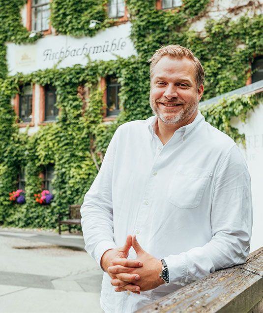 Herr Max Kaub lächelnd vor dem aktuellen Gebäude der Fischbachsmühle